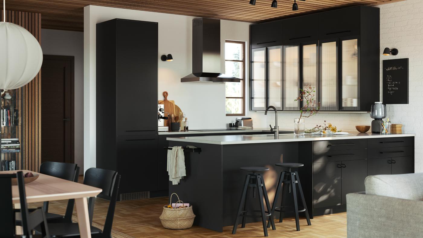 Una cocina con frentes NICKEBO, gabinetes con puertas HEJSTA de cristal de en vidrio de carbón/caña y bancos altos DALFRED en negro.