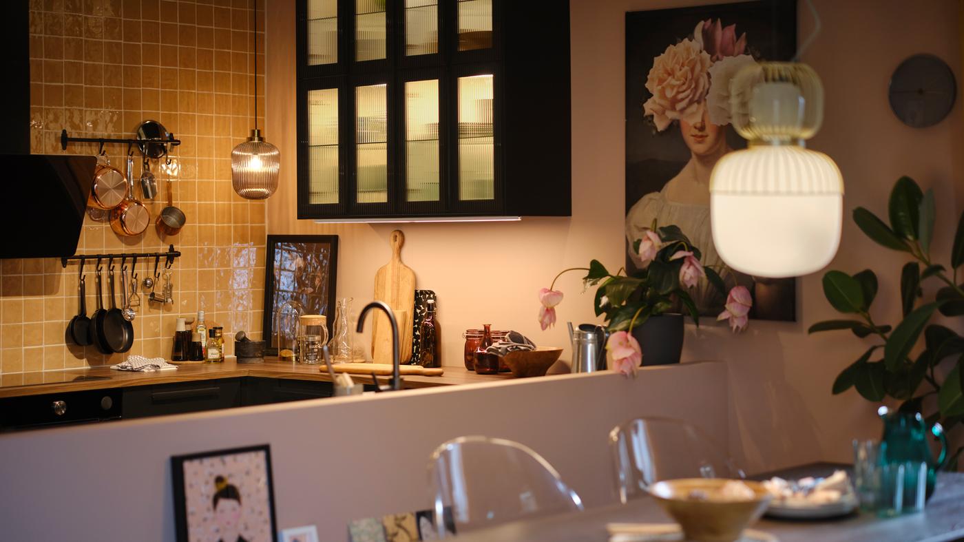 Una cocina con muebles altos con puertas de vidrio e iluminación en el interior, además de lámparas colgantes sobre una mesa.