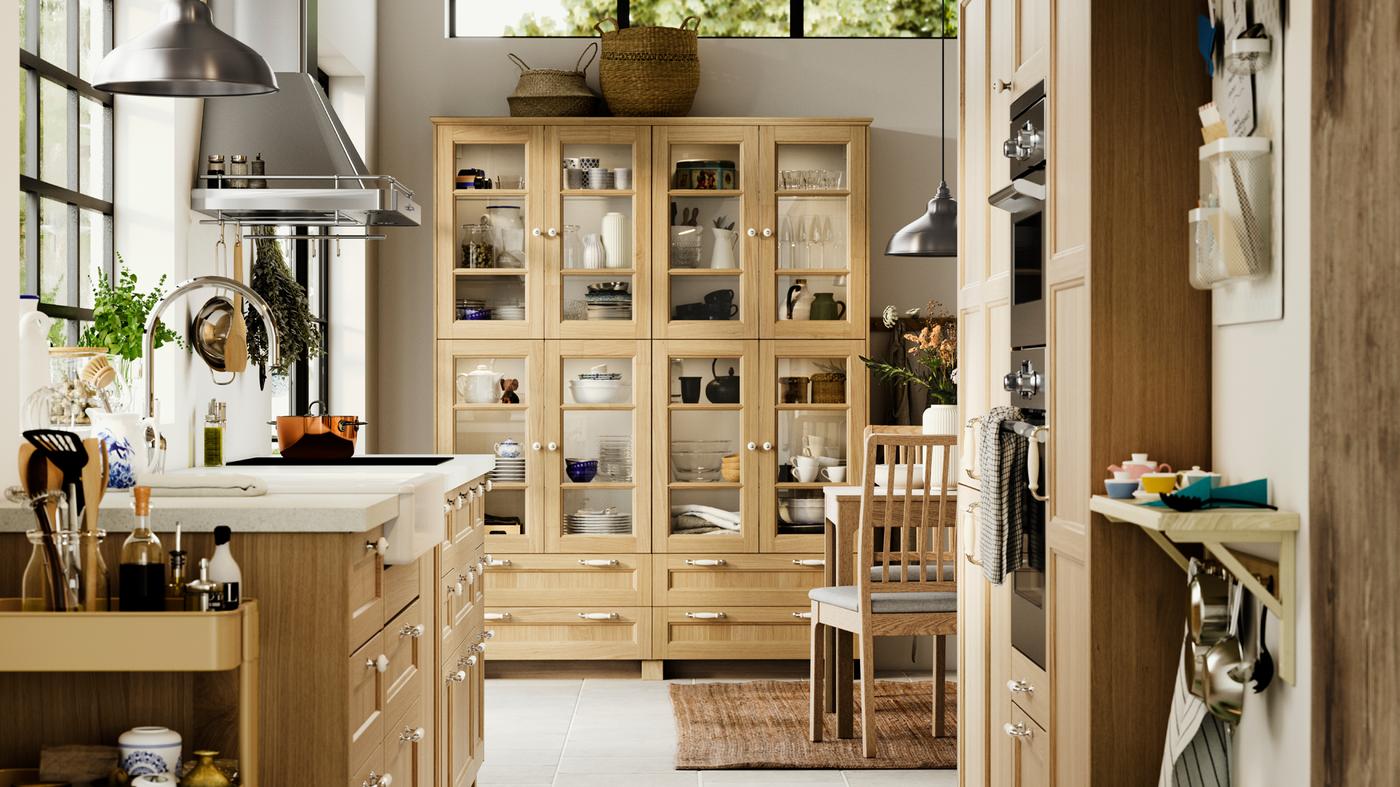 Una cucina con frontali FORSBACKA in impiallacciatura di rovere, una vetrina e un piano di lavoro SÄLJAN bianco effetto pietra/laminato - IKEA.