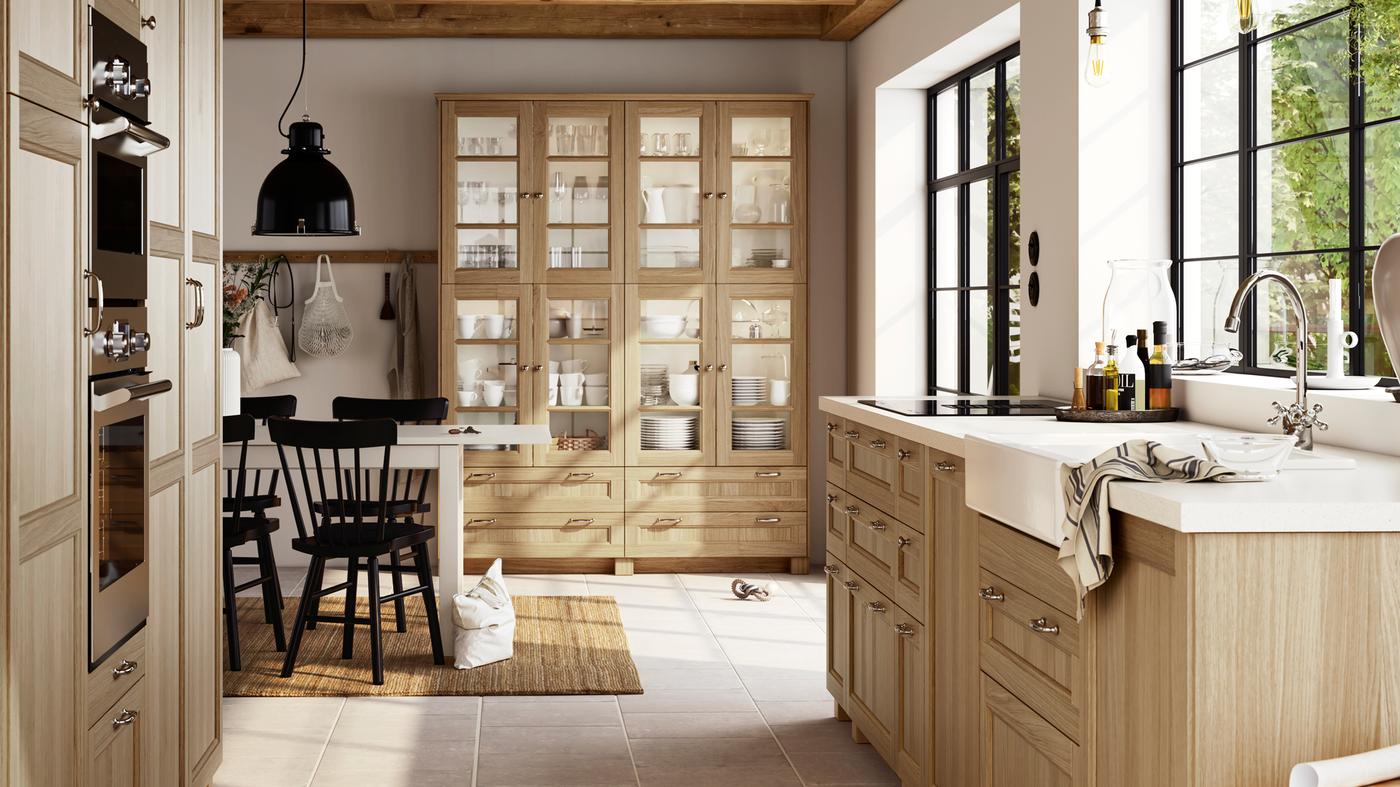 Una cucina grande e luminosa con frontali VEDHAMN in noce e vetrine con stoviglie e articoli in vetro.