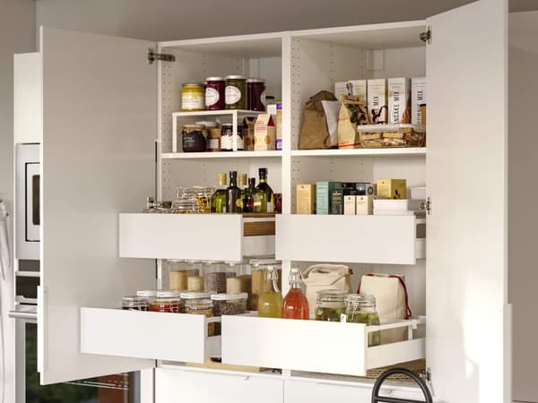 Una despensa de cocina blanca organizada de forma prolija con estantes abiertos y cajones extraíbles que contienen frascos, aceites, productos secos y condimentos.