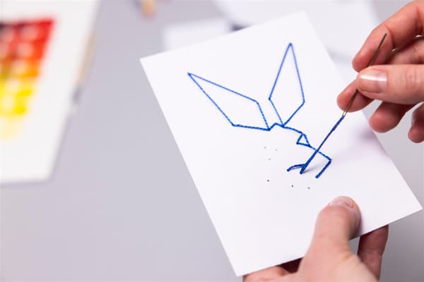 Una donna infila un filo in un foglio di carta e ne ricava un coniglio.