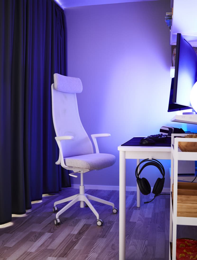Una estación gaming con una silla gamer JÄRVFJÄLLET blanca frente a un escritorio gamer blanco. La habitación está iluinada con tonos azules.