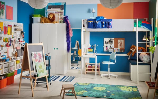 Una habitación colorida de niños con una cama loft, una alfombra con patrones de hojas y una silla de escritorio infantil azul.