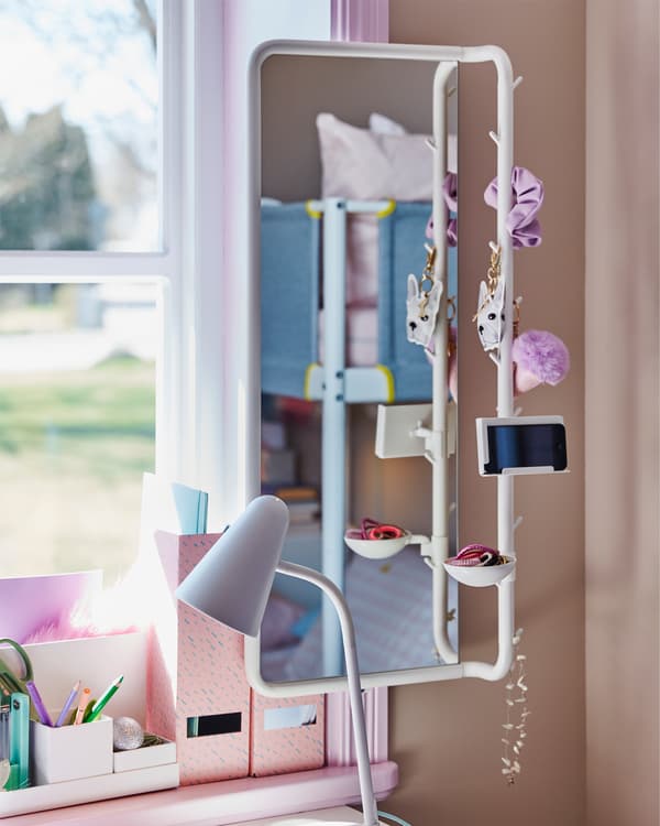 Una habitación infantil con un acercamiento al espejo blanco MÖJLIGHET que sostiene un teléfono, accesorios para el cabello y un collar.