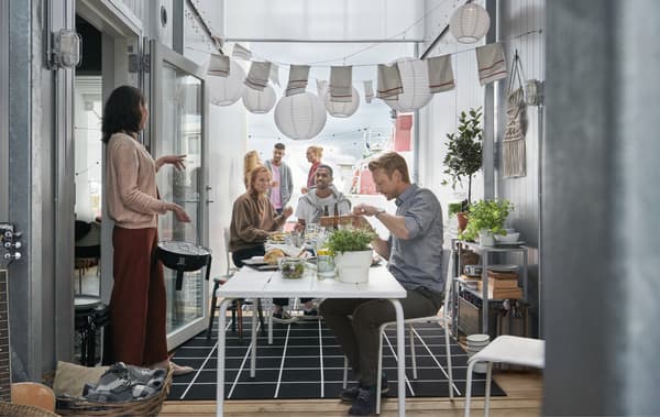 Una lunga tavola apparecchiata in uno spazio tra due container, decorato con lanterne di carta – IKEA