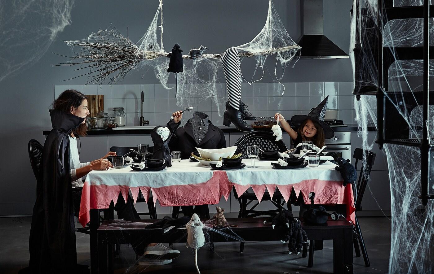 Una mamma e i suoi bambini, in costume, sono seduti a un tavolo addobbato per Halloween con ragnatele e decorazioni da brivido.