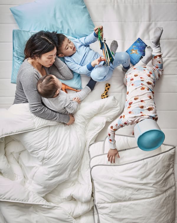 Una mamma legge una storia dal libro illustrato DJUNGELSKOG insieme ai suoi tre bambini, sotto il piumone di un letto matrimoniale - IKEA
