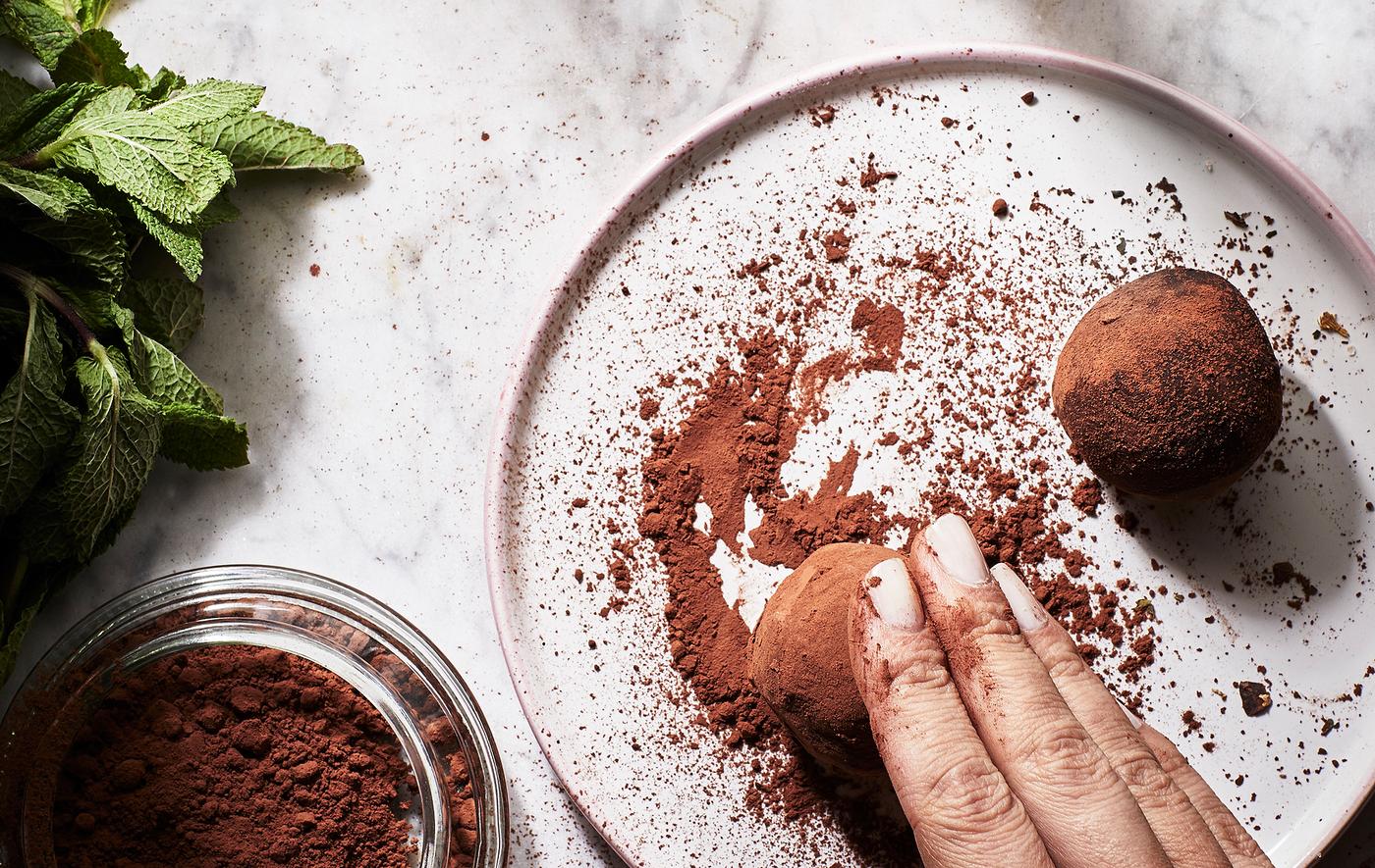 Una mano passa delle palline in un piattino con del cacao in polvere per formare dei tartufi; foglie di menta fresca sul lato - IKEA