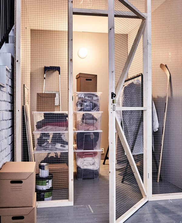 Una mansarda con contenitori di plastica trasparenti e impilabili, scatole di cartone e uno stand appendiabiti per organizzare i vestiti invernali - IKEA.