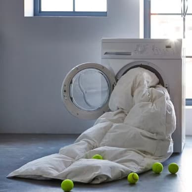 Una máquina de lavar centrifuga con un plumón que sobresale por la puerta, se ven unas pelotas de tenis esparcidas por el piso.