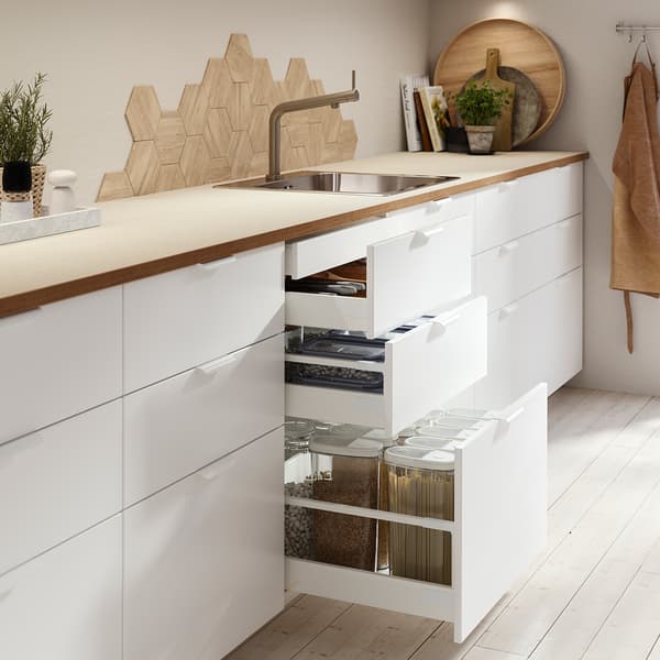 Una moderna cucina bianca con un piano di lavoro in quercia, con cassetti aperti con organizer e contenitori. 
