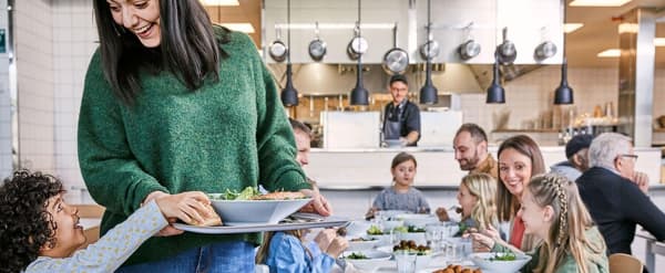 Una mujer con un suéter verde junto a otras personas sosteniendo una bandeja de comida
