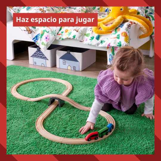 Una niña juega con un tren de madera IKEA sobre una alfombra  infantil.