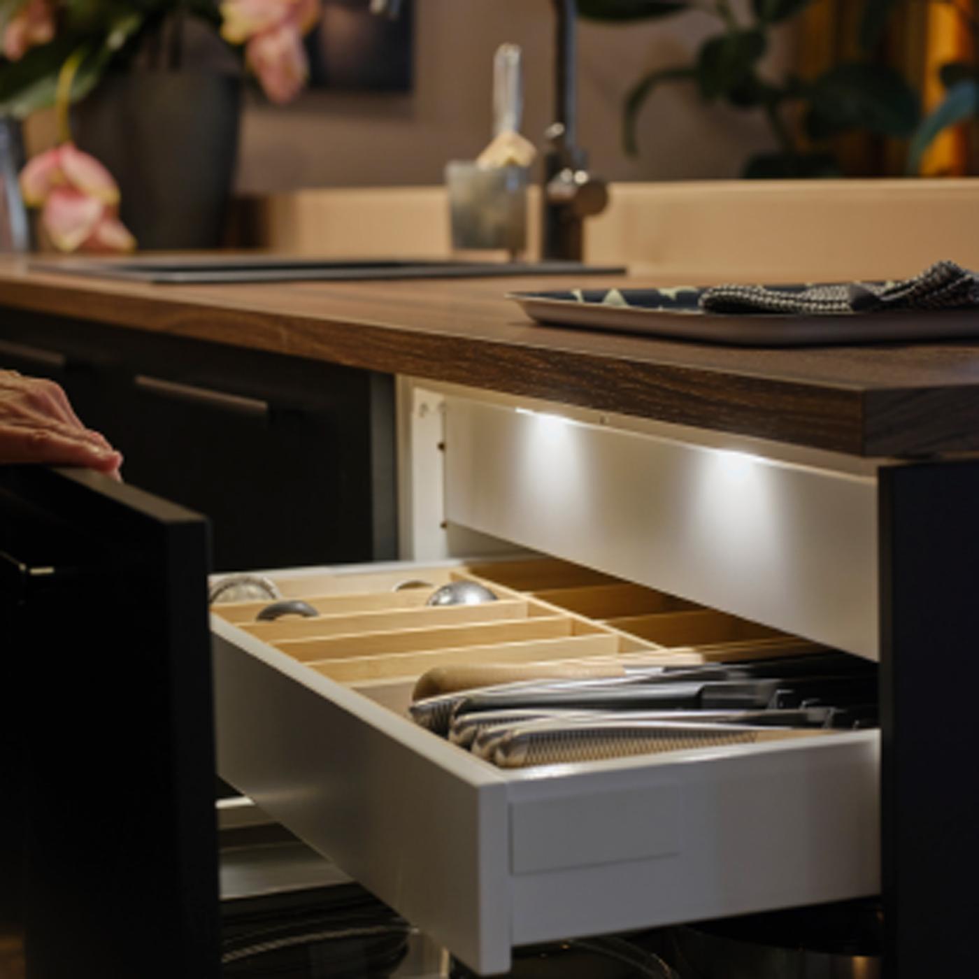 Una persona apre un cassetto di una cucina con un frontale antracite opaco al cui interno c'è un'illuminazione a LED MITTLED con sensore integrato.