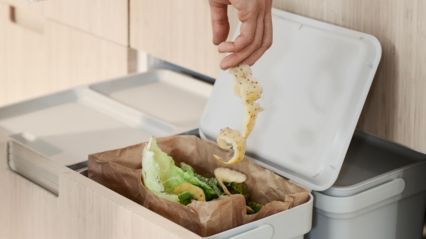 Una persona echa cáscara de verdura en una bolsa de papel marrón para residuos de alimentos en un contenedor de clasificación de residuos HÅLLBAR dentro de un cajón alto MAXIMERA.