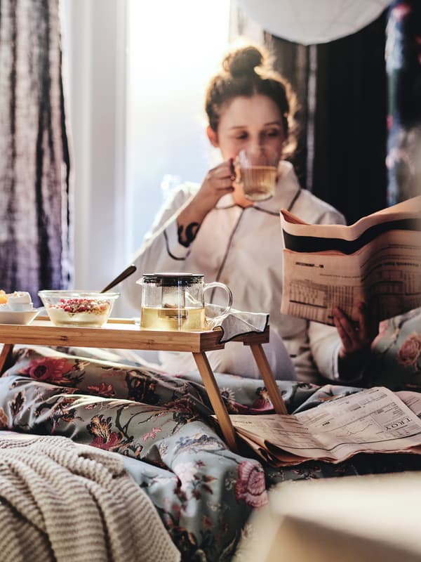 Una persona está tomando desayuno en una cama con un plumón con funda nórdica floral de color gris verdoso claro.