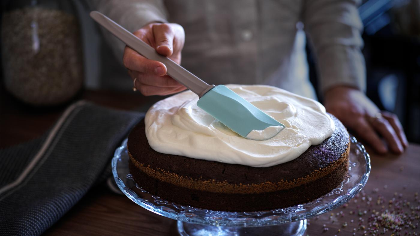 Una persona glassa una torta con una spatola di gomma BAKGLAD - IKEA