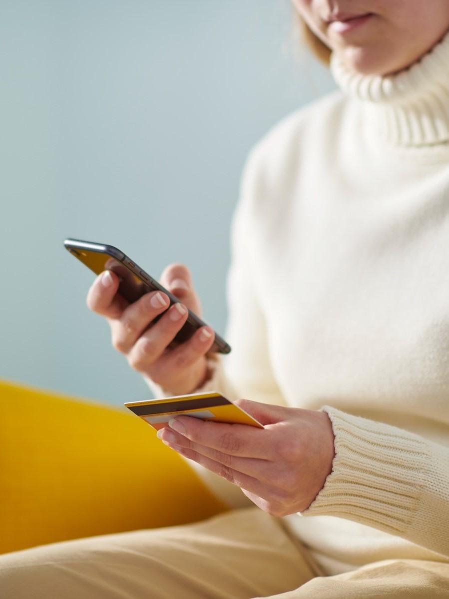 Una persona tiene una carta bancaria in una mano e uno smartphone nell’altra. 