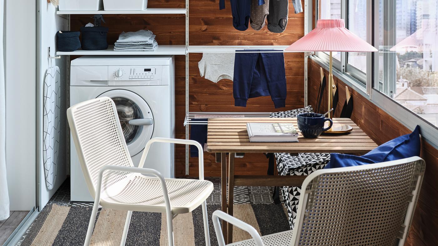 Una piccola veranda con una parete attrezzata a lavanderia bianca, una lavatrice, un tavolino e due sedie bianche/beige - IKEA