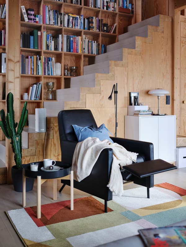 Una poltrona reclinabile GISTAD nera con sopra un plaid in una stanza con pareti in legno, con il poggiapiedi in posizione reclinata - IKEA