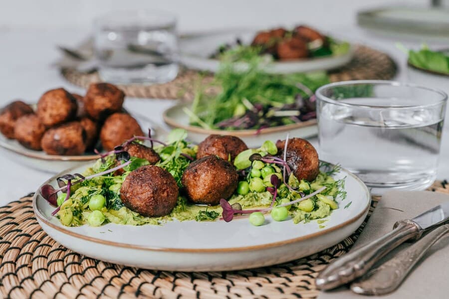 Una preparación vegana con albóndigas vegetales HUVUDROLL y hummus de espinaca sobre un plato cerámico GLADELIG beige. 