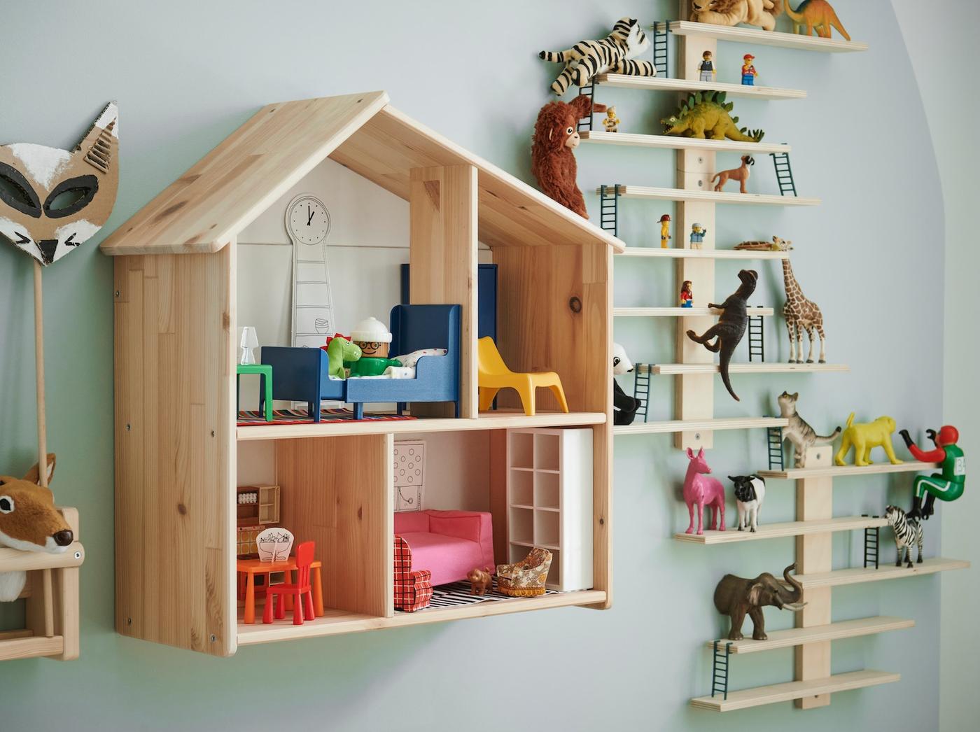 Una repisa en forma de casa de muñecas FLISAT con muebles en miniatura HUSET, junto a una repisa de madera escalonada con figuras de animales. 