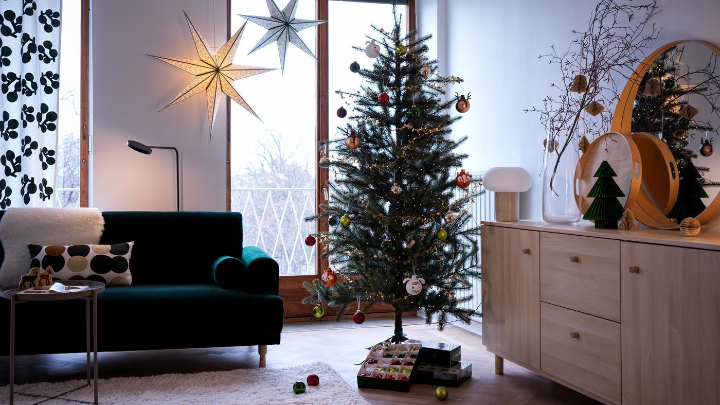 Una sala con un árbol de Navidad decorado junto a un sofá verde y estrellas colgantes.