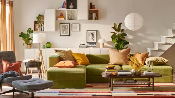 Una sala con un gran sofá en l , una mesa de centro y muchos muebles. En la pared hay repisas EKET de muchos colores.