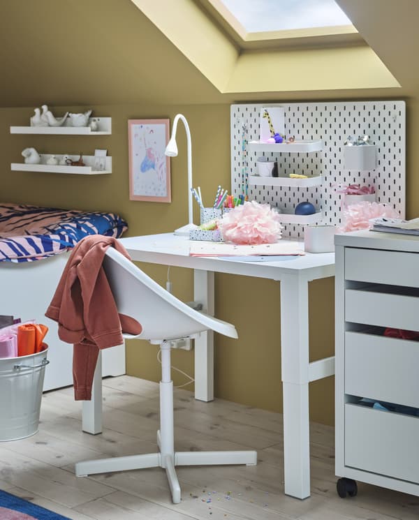Una scrivania bianca, una sedia girevole per bambini, una cassettiera, un pannello portaoggetti montato a parete e una lampada da lavoro a LED bianca - IKEA