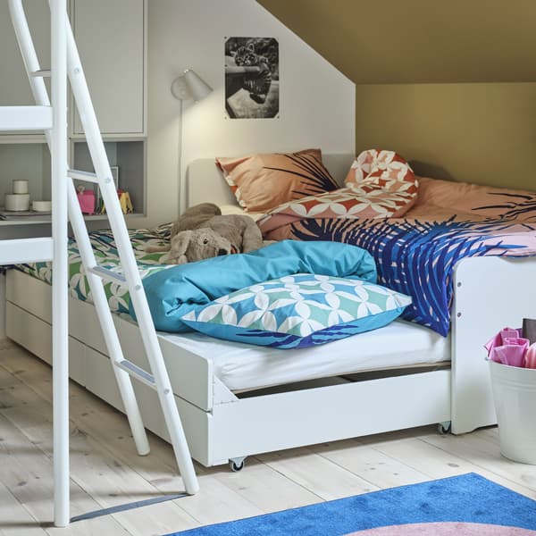 Una struttura letto bianca con biancheria a motivi rosa, un letto extra estratto con biancheria a motivi blu e un peluche a forma di cane - IKEA