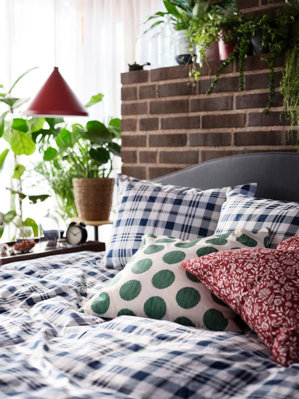 Una struttura letto imbottita HAUGA con un copripiumino a quadri, un cuscino a pois verdi e uno rosso a fiori - IKEA