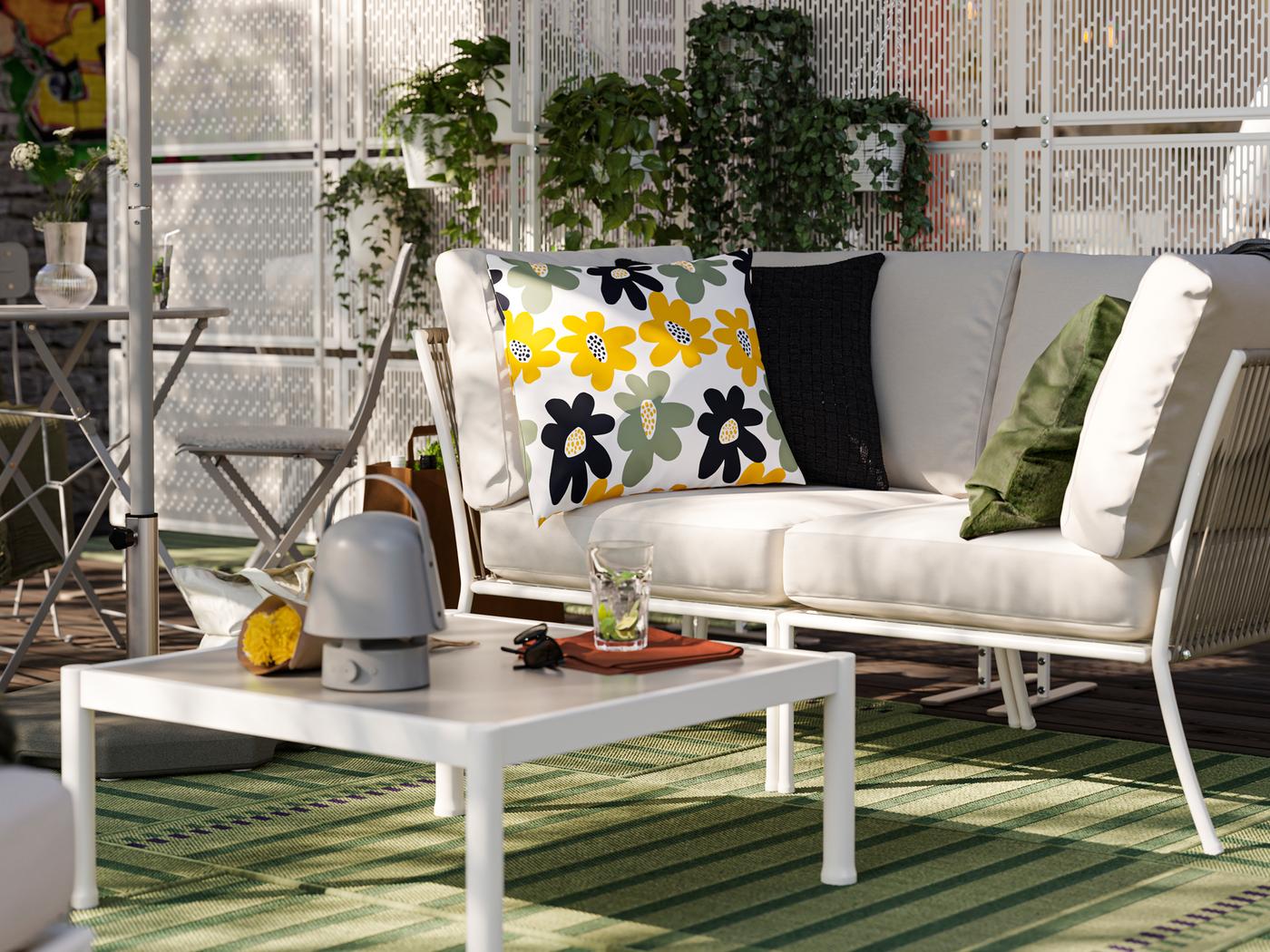 Un'area relax all'aperto con un divano e un tavolo SEGERÖN, tappeti da esterno verdi e paraventi con piante - IKEA.
