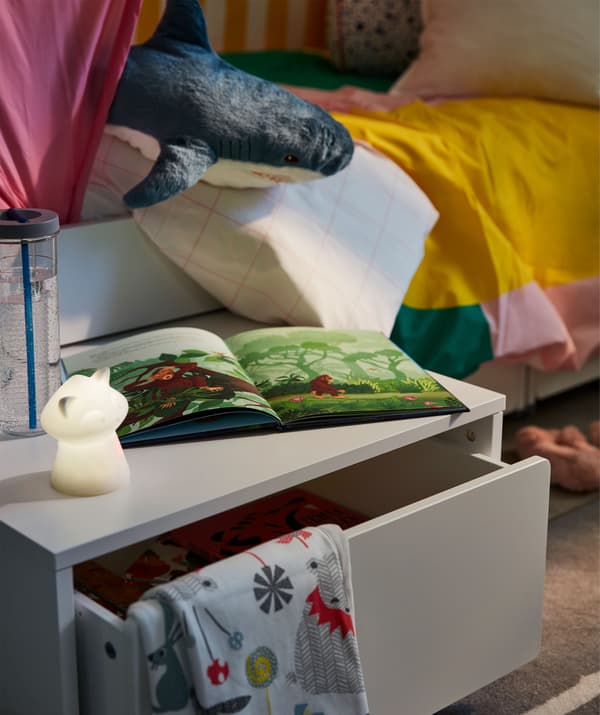Under-bed storage box on castors drawn out to form a bedside table. On the table a night light, book, water bottle.