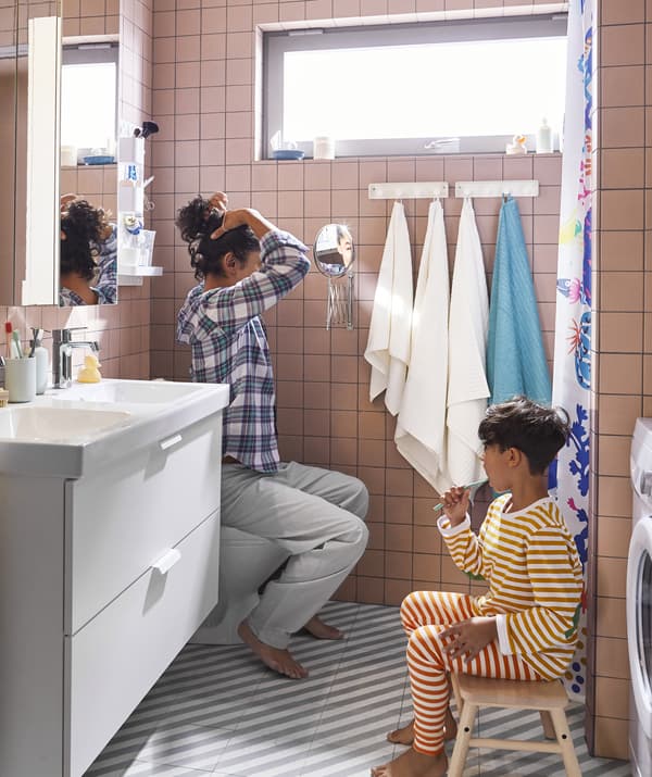 Une adulte et un enfant dans la salle de bains équipée d’un lavabo double, d’un tabouret et de deux miroirs.