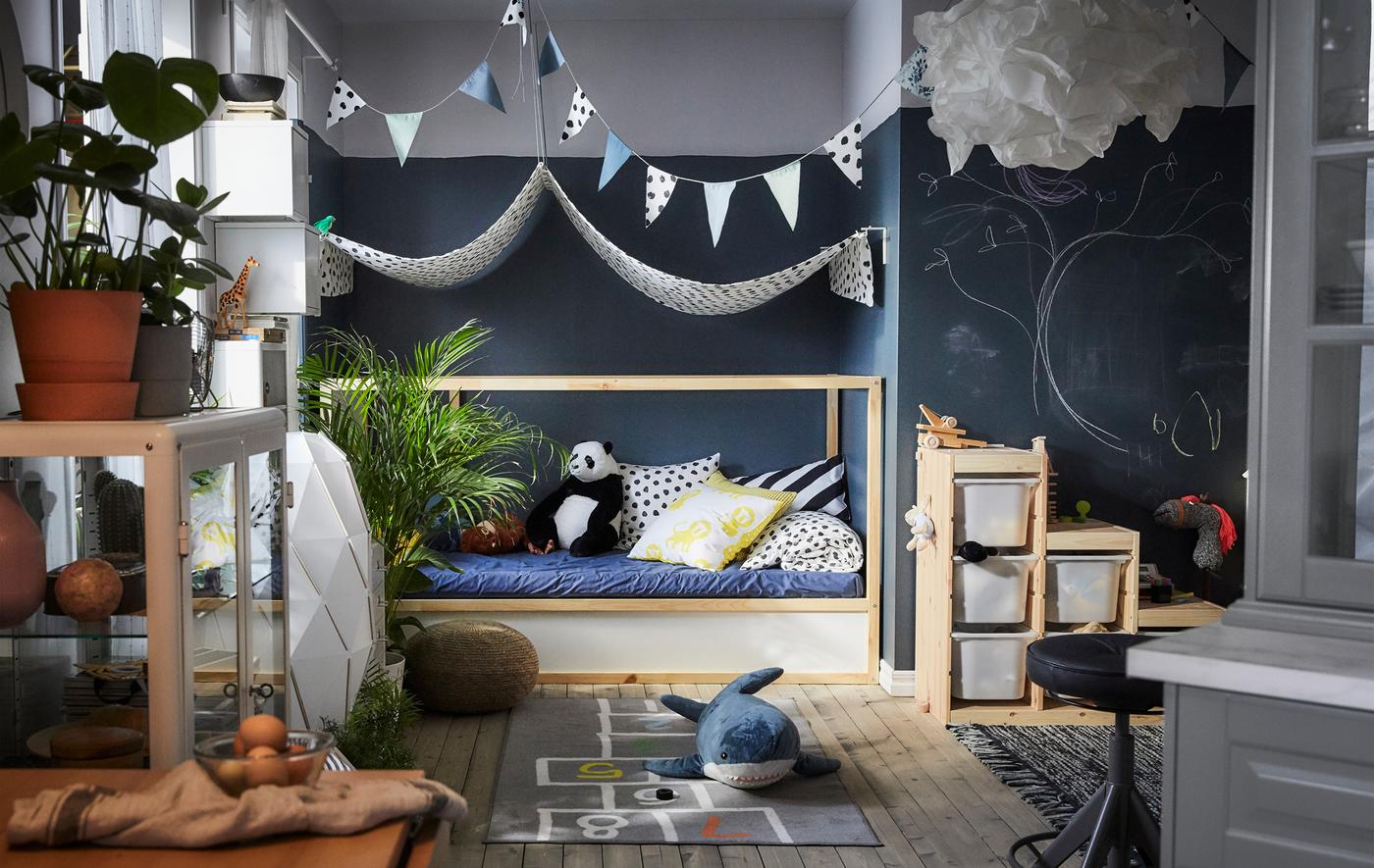 Une aire de jeu, un ciel de lit en tissu au-dessus d’un lit d’appoint, des tapis avec des motifs et des boîtes de rangement.