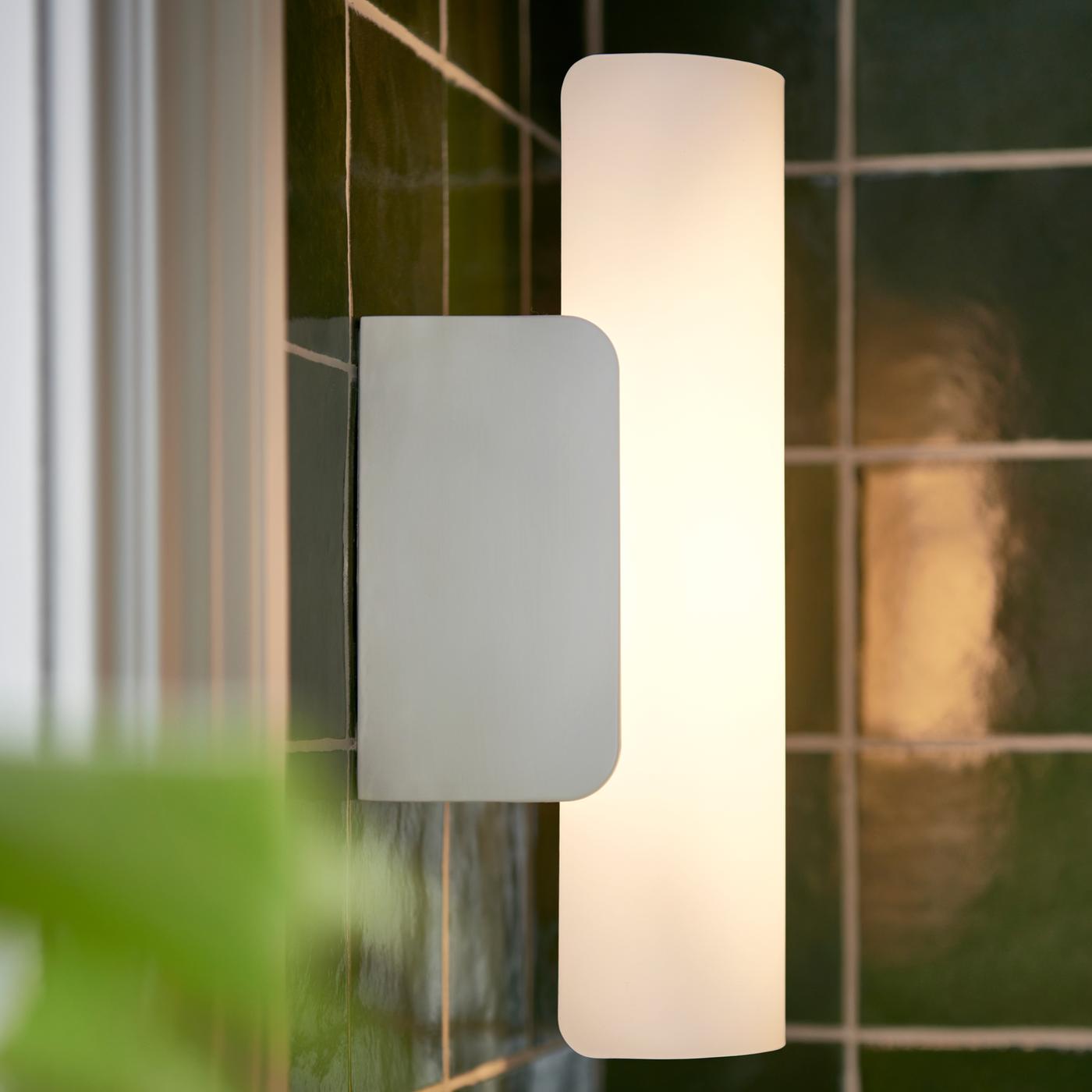 Une applique à DEL HAVSDUN blanc en verre dépoli blanc et à intensité lumineuse réglable éclaire une salle de bains carrelée de vert.