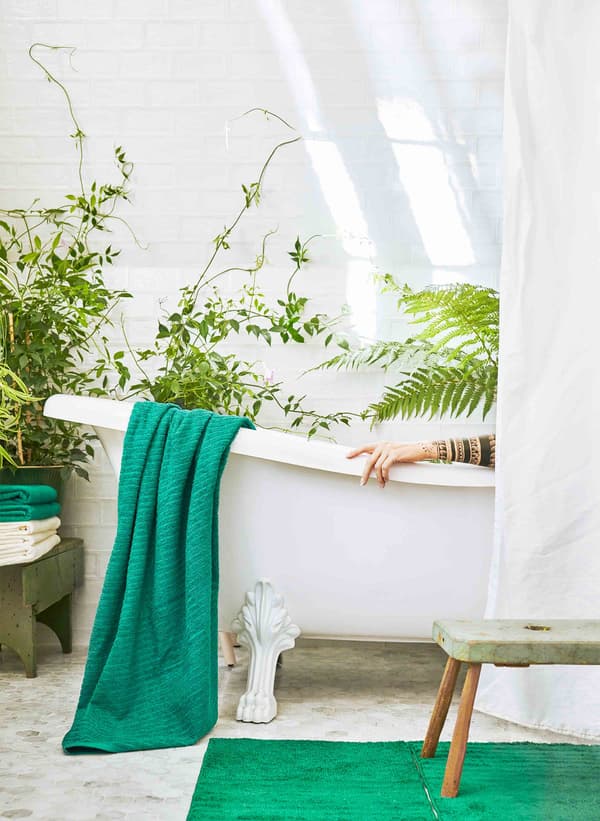 Une baignoire blanche dans une salle de bain remplie de plantes vertes, à moitié cachée par un rideau blanc.