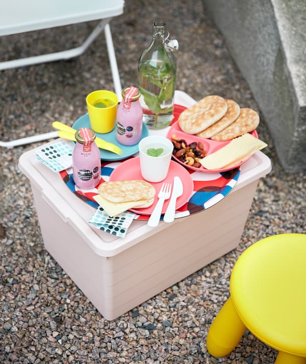 Une boîte rose SOCKERBIT fait office de petite table avec de la vaisselle HEROISK, placée entre une chaise FEJAN et un tabouret MAMMUT.