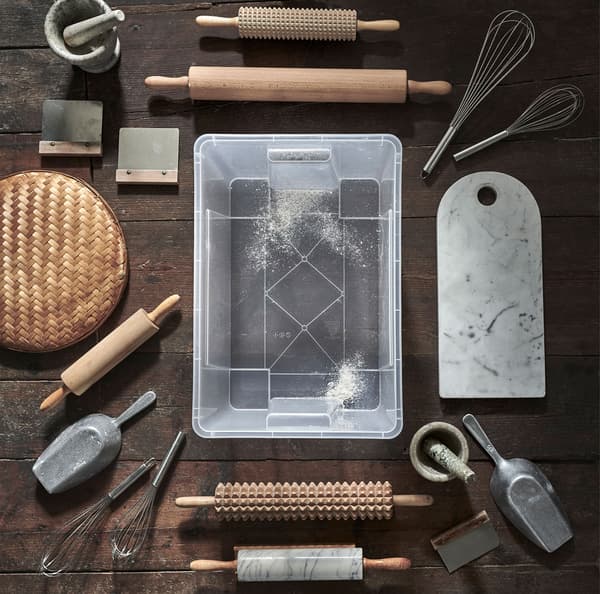 Une boîte transparente SAMLA sur un plancher de bois, entouré de divers accessoires à pâtisseries.