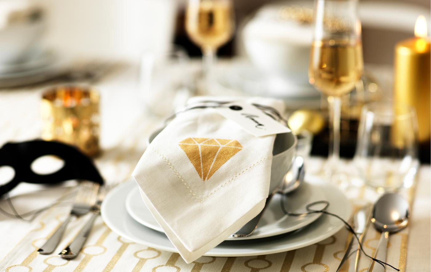 Une bonne idée pour décorer la table consiste à personnaliser des serviettes en tissu. Avec, par exemple, un motif de diamant doré peint au pochoir sur des serviettes blanches GULLMAJ de chez IKEA. Posez-les ensuite sur les assiettes et les bols blancs, sur un set de table blanc et doré.