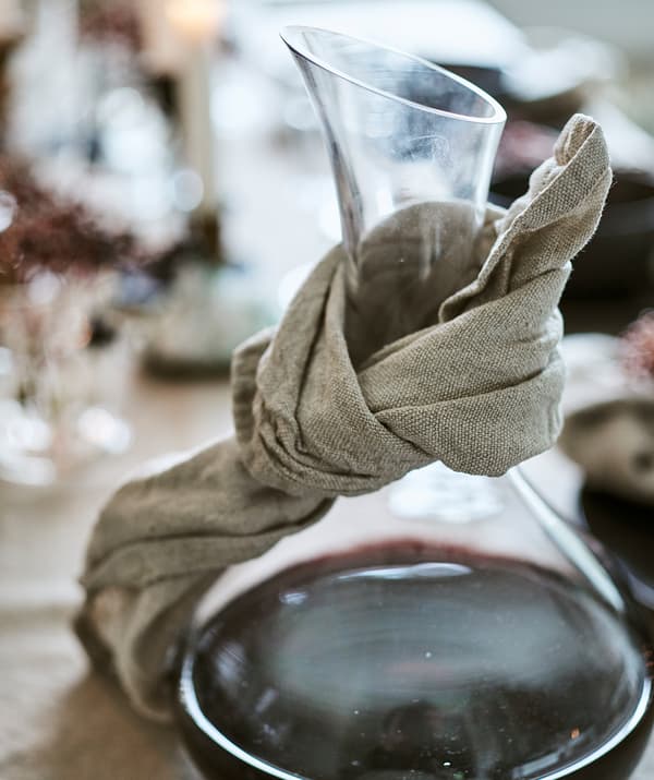 Une carafe en verre avec du vin rouge enroulée dans une serviette en lin pour récolter les gouttes.