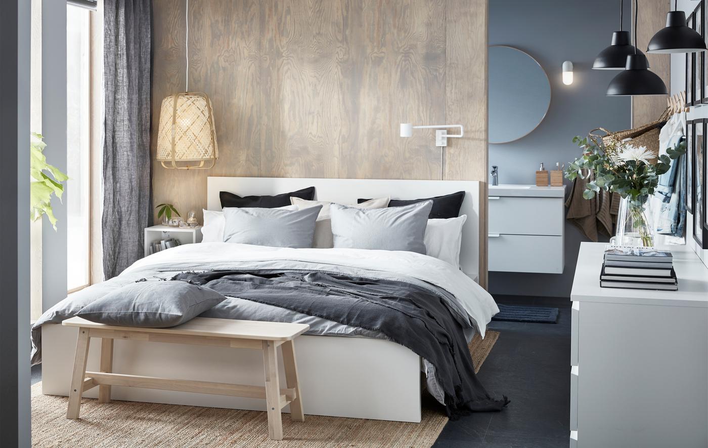 Une chambre à coucher dans les tons neutres, un lit double, un banc en bois et une lampe en osier.