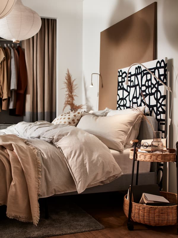 Une chambre avec un cadre de lit rembourré SLATTUM et des housses de couette et taies d’oreiller BERGPALM beiges.