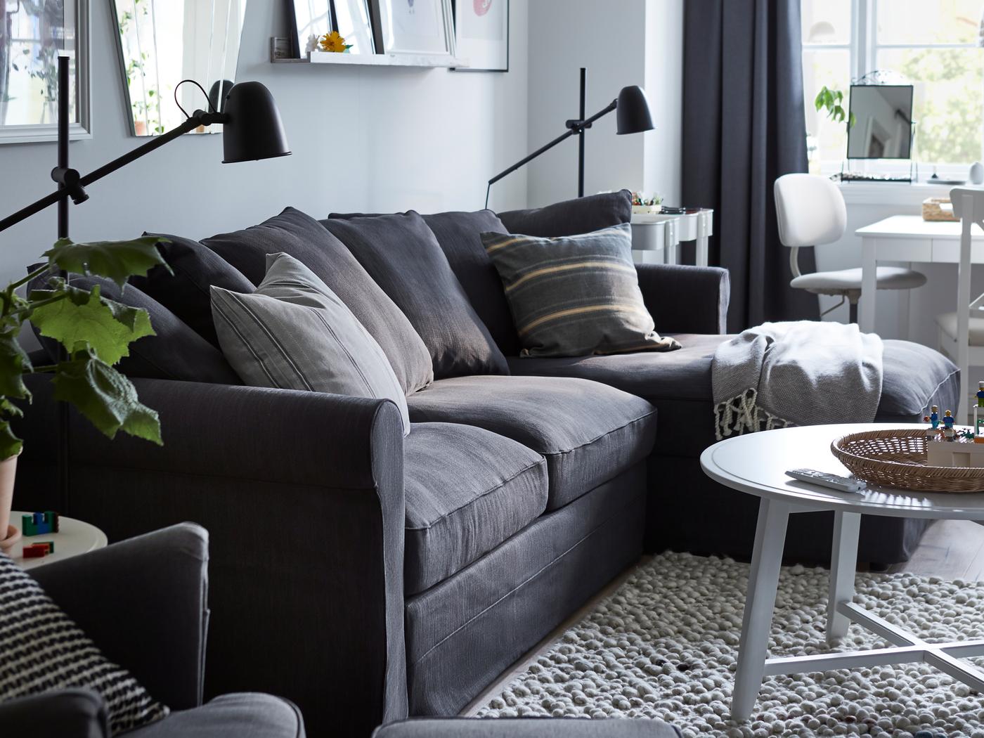 Une chambre avec un canapé-lit GRÖNLID avec chaise longue, deux lampadaires/liseuses SKURUP noirs et différents tableaux au mur.