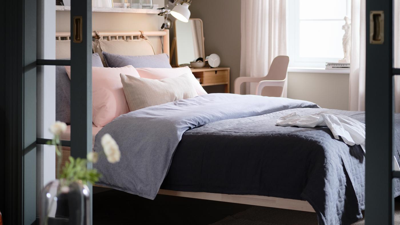 Une chambre avec un lit en bouleau BJÖRKSNÄS, des draps de lit KOPPARBLAD bleu foncé, une coiffeuse NORDKISA et une chaise pivotante ODGER.