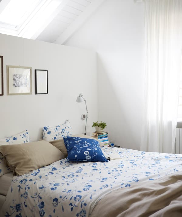 Une chambre blanche avec un linge de lit bleu et blanc et un puits de lumière.