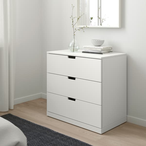 Une chambre épurée au design scandinave, avec une commode blanche IKEA NORDLI, quelques livres et un vase.