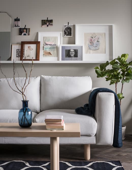 Une cimaise placée au-dessus du canapé reçoit photos et œuvres d’art. De plus petites photos sont accrochées avec du ruban adhésif décoratif.