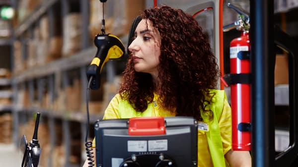 Une collaboratrice IKEA aux longs cheveux foncés conduit un élévateur à fourches dans la zone Libre-service.